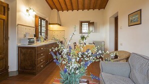 A cozy kitchen with wooden cabinets, a dining area with a table and chairs, and a living room with a striped sofa. - Casa Bonannia A: A cheerful one-story apartment in the characteristic style of the Tuscan countryside. (Bagno a Ripoli)