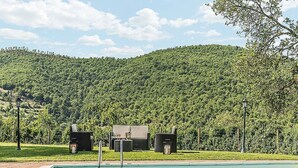 Piscina con sillas de descanso y una mesa, rodeada de un jardín ajardinado y una colina al fondo.