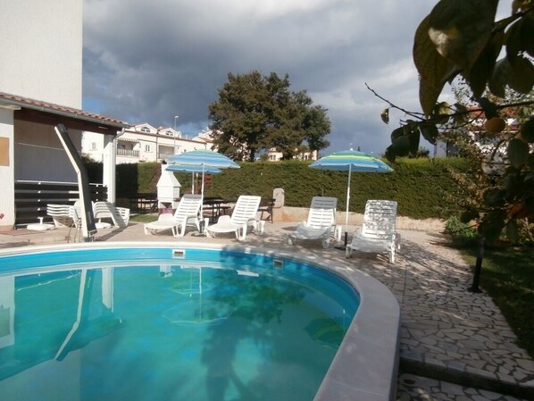 A swimming pool with lounge chairs and umbrellas, surrounded by a landscaped garden and a building. - Apartment in Poreč with Balcony, Air condition, WIFI (819-5) (Porec)