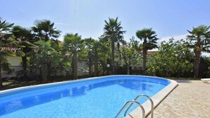 A swimming pool with a tiled edge, surrounded by palm trees and a stone patio. - Apartment in Poreč with Balcony, Air condition, WIFI (819-5) (Porec)
