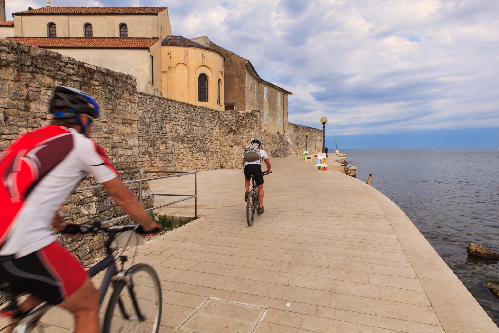A paved walkway beside a body of water with stone walls and a building in the background.
