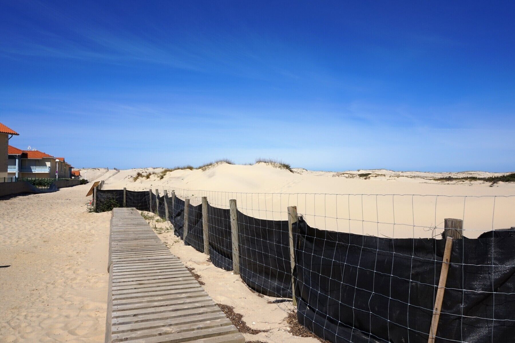 A sandy beach with a wooden boardwalk and a fence.