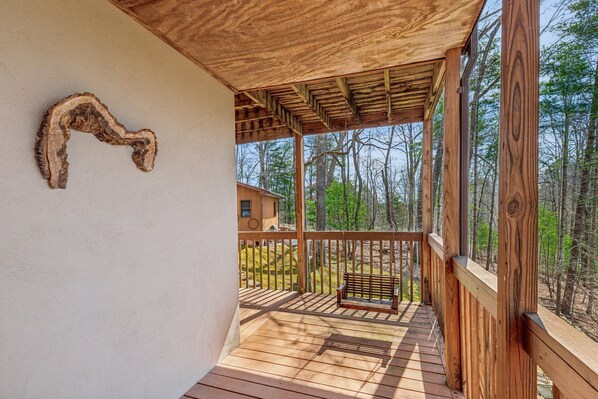 Une terrasse en bois avec un banc, une rambarde en bois et une vue sur une zone boisée.