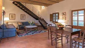 Amplia sala de estar con una escalera de madera, una mesa de comedor con sillas, un sofá y una mesa auxiliar.