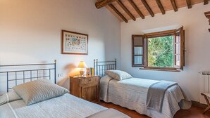 Un dormitorio con dos camas, una mesita de noche con lámpara, un mapa enmarcado en la pared y una ventana con persiana abierta.