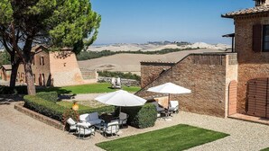 Un patio con mesas al aire libre, un muro de piedra y vistas a colinas ondulantes.