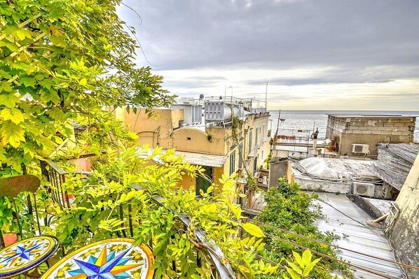 A rooftop terrace with a view of the sea, surrounded by buildings with balconies and some greenery.