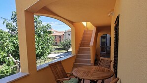 A balcony with a wooden table and chairs, a view of a staircase, and a window overlooking a garden. - Apartment in Stivan with Terrace, Air condition, WIFI (920-2) (Stivan)