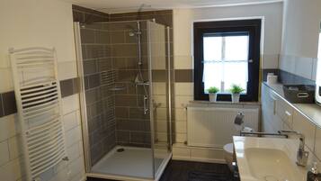 Une salle de bain moderne avec une douche à parois de verre, un lavabo blanc et une fenêtre agrémentée de plantes.