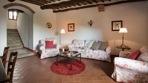 A cozy living room with a staircase, floral-patterned sofas, a coffee table, and wall-mounted lamps. - Montestigliano, an authentic farmhouse in the heart of Tuscany, is an oasis of peace and beauty that offers its guests refined residences and an enchanting view (Rosia - Sovicille)