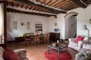 Una sala de estar acogedora con chimenea, un comedor con sillas de madera, una estantería y un sofá floral.