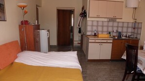A hotel room with a bed, a small kitchenette, a wooden chair, and a table. - Apartment in Baška with Terrace, Air condition, WIFI, Washing machine (863-3) (Baška)