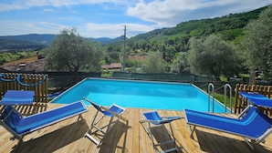 Una terrazza in legno con piscina, immersa nel verde e circondata da colline.