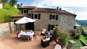 Una casa in pietra con tetto in tegole, un patio con tavolo apparecchiato per mangiare, mobili da esterno e piante in vaso.