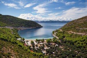 A coastal area with a beach, parked vehicles, and a clear view of the sea and distant mountains.