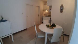 Un área de comedor compacta con una mesa redonda, dos sillas y una mesita auxiliar con una planta.
