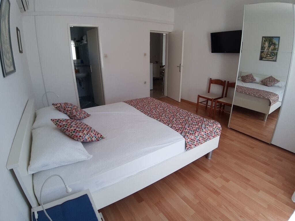 Una camera da letto con un letto, una sedia, una TV e uno specchio.