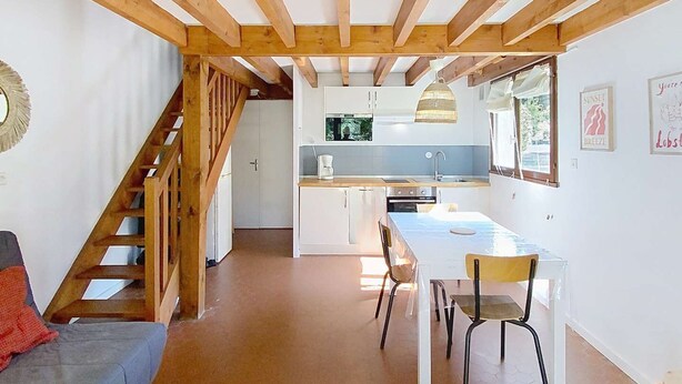 A spacious living area with a high wooden ceiling, a kitchen in the background, and a staircase leading to an upper level.