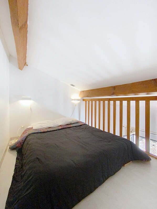 Un dormitorio con cama, viga de techo de madera y balcón con barandilla.