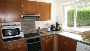 A modern kitchen with wooden cabinets, a built-in oven, a coffee maker, and a window with a view of greenery. - House 3 bedrooms, 6 people in a residence with pool in Lacanau ocean (LACANAU OCEAN)