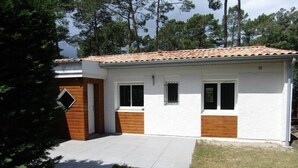 A single-story house with a tiled roof, white exterior walls, and wooden accents around the windows and door. - House 3 bedrooms, 6 people in a residence with pool in Lacanau ocean (LACANAU OCEAN)