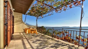 Un balcone con tavolo e sedie, affacciato su un lago e montagne.