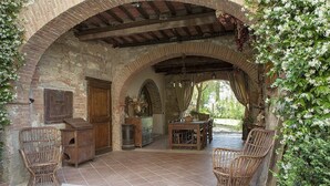 A rustic outdoor patio with brick arches, wicker furniture, a wooden table, and a stone fireplace.