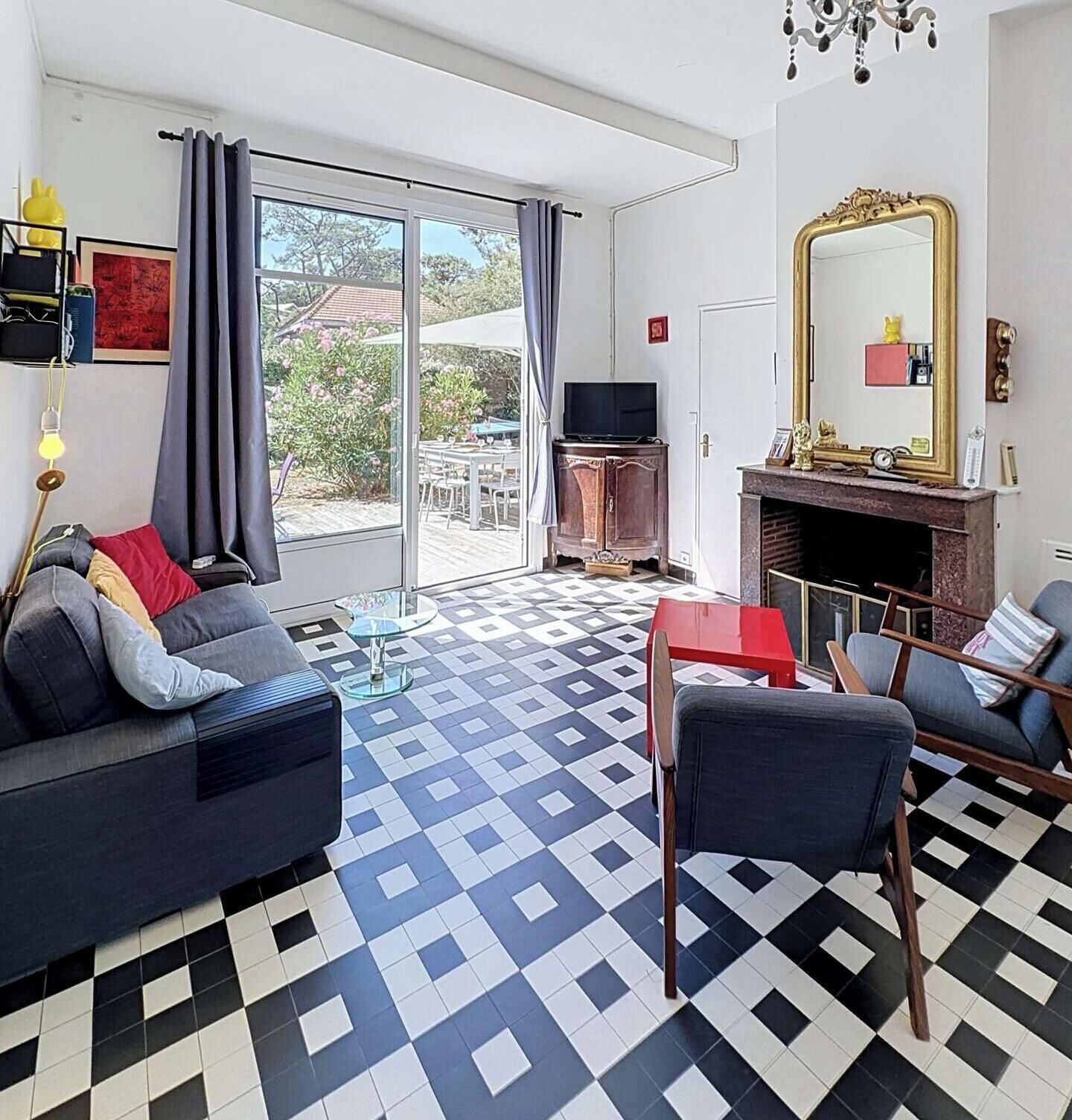 A living room with a checkered floor, a sofa, a chair, a television, a fireplace, and a large window with curtains.