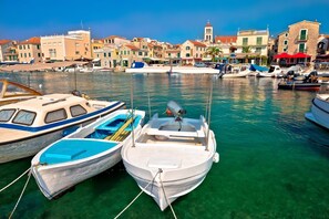 A marina with boats docked, clear water, and buildings in the background.