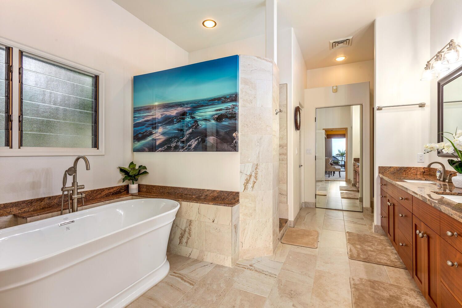 A modern bathroom with a freestanding bathtub, a large painting of a coastal scene, and a view into the adjacent living area.