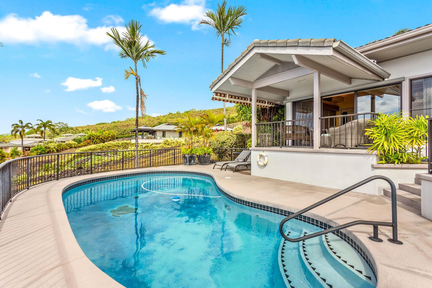 A swimming pool with a curved design, surrounded by a metal fence and a covered patio area.