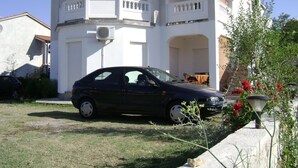 A two-story building with a balcony, a parked car, and a garden with red flowers. - Apartment in Lopar with Terrace, Air condition, WIFI (568-4) (Lopar)