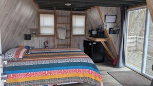 A bedroom with a bed, a desk, a chair, a fire extinguisher, and a window. - A-Frame Tiny House Tucked into the Northwoods (Walker)