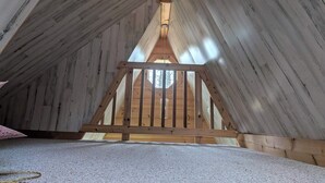 An attic room with wooden slats on the ceiling and a wooden railing. - A-Frame Tiny House Tucked into the Northwoods (Walker)