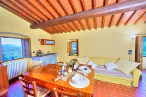 Un coin repas chaleureux avec une table en bois dressée pour deux personnes, un canapé et une vue sur l’extérieur.