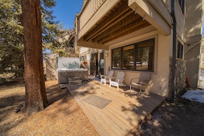 Une terrasse en bois avec des sièges d’extérieur, un jacuzzi et un mur en pierre.
