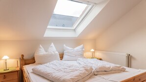 Een slaapkamer met een schuine kap en dakraam, houten bedframe, witte beddengoed en bedlampjes.