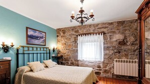 Ein Schlafzimmer mit Steinwand, Holzboden, einem Bett mit Kopfteil, einer Chandelierleuchtre, einem Heizkörper und einem Fenster mit Vorhängen.