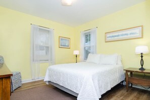 A bedroom with a large bed, two bedside lamps, a framed picture on the wall, and a window with a curtain.