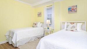 Ein Zimmer mit zwei Einzelbetten, einem kleinen Tisch mit Lampe und einem Fenster mit Jalousien.