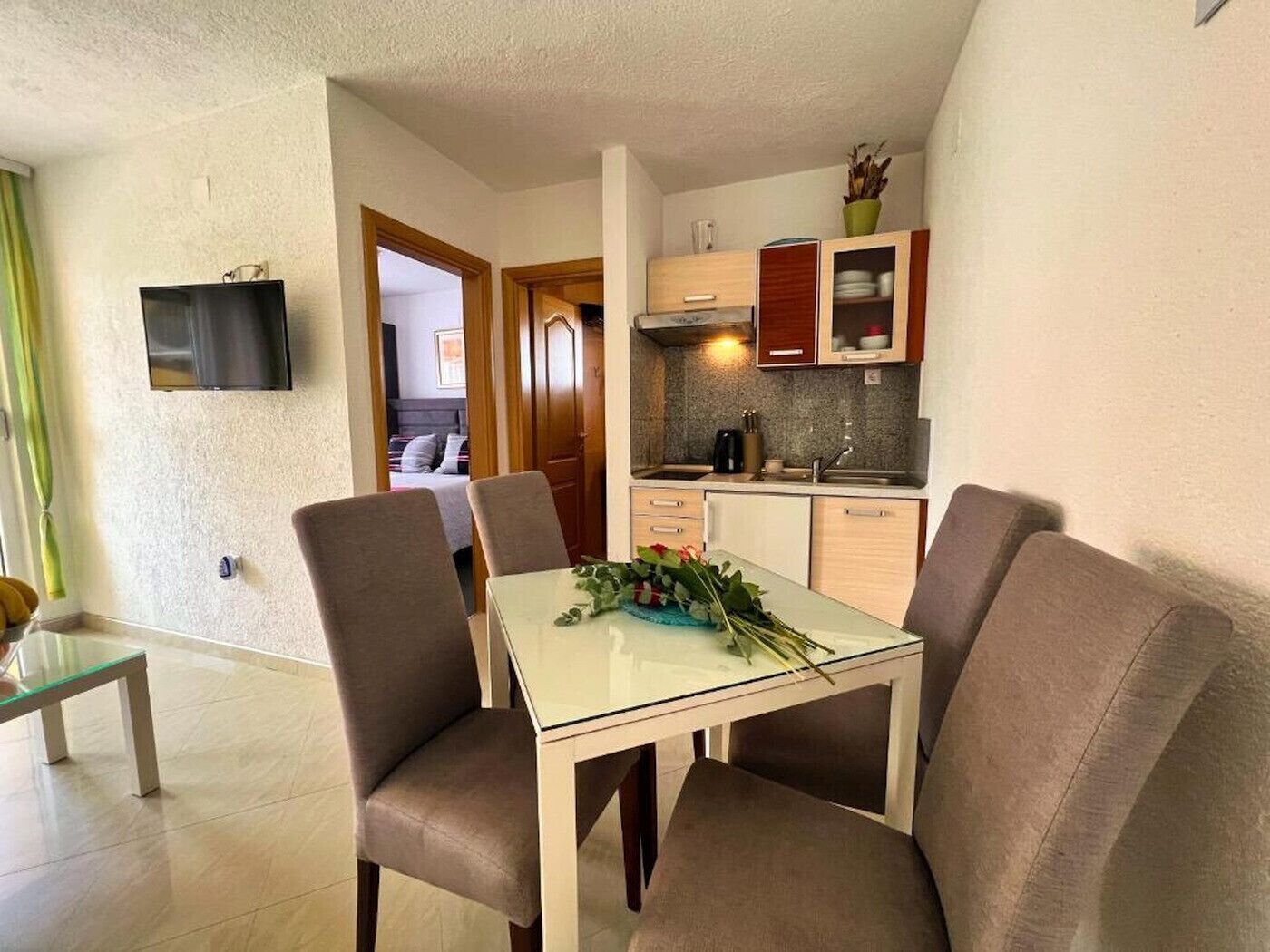 A compact living space with a dining area, kitchenette, and a bedroom visible through an open door.