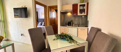A compact living space with a dining area, kitchenette, and a bedroom visible through an open door.