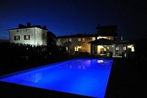 A nighttime view of a pool area with a lit-up pool, a stone building, and a well-lit house in the background. - Villa Vezzosa D: A cozy and welcoming apartment that is part of an ancient country house, with Free WI-FI. (Citerna)