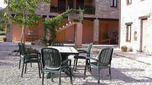 Un edificio con fachada de piedra, una escalera que lleva a un balcón y mobiliario exterior con sillas y una mesa.