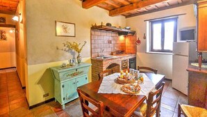 Una cocina rústica con un horno de ladrillo, vigas de madera en el techo, una mesa de comedor para cuatro personas y un aparador azul antiguo.
