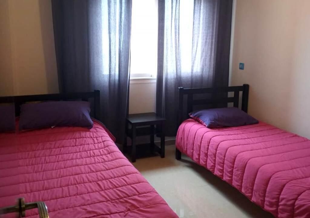 Habitació amb dos llits individuals, cadascun amb estructura de fusta i roba de llit rosa. Hi ha una taula petita entre els llits i una finestra amb cortines.