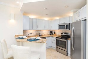 A modern kitchen with white cabinets, a stainless steel refrigerator, a built-in oven, a microwave, and a coffee maker.