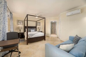 A four-poster bed with a canopy, a desk with a chair, a sofa, and a shower area.