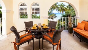 A dining area with wicker chairs and a table set for four, overlooking a tropical beach. - Modern Beachfront Condo with Pool - Sapphire 118 (Saint Lawrence Gap)