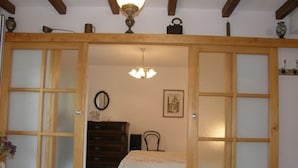 Une pièce comprenant une armoire en bois, un lit recouvert d’une couvre-lit à motifs floraux, une commode, une chaise et un luminaire suspendu.
